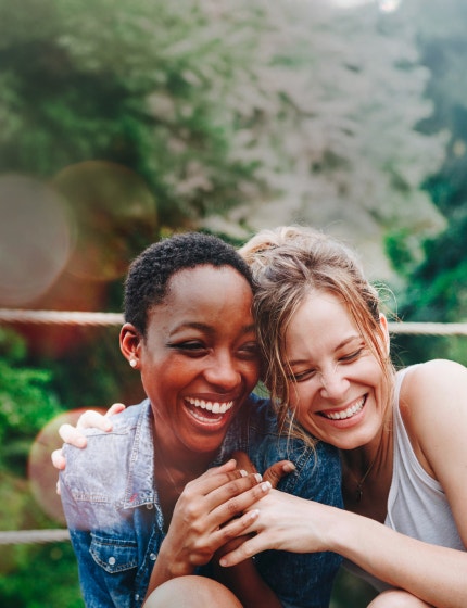 A black woman and a white woman smiling together, showing support and companionship in managing inflammatory bowel disease.