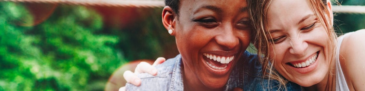 A black woman and a white woman smiling together, showing support and companionship in managing inflammatory bowel disease.